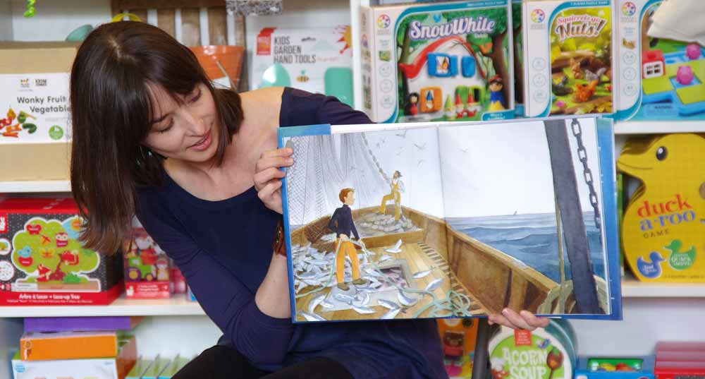 Photograph of Jessica Lanan reading a copy of 'The Fisherman and the Whale' at a story time event